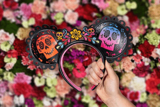 Orejas de Mickey con diseño del Día de los Muertos sostenidas frente a fondo de flores