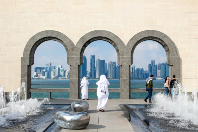 Personas caminando en el Museo de Arte Islámico de Doha con vista al skyline de Qatar.