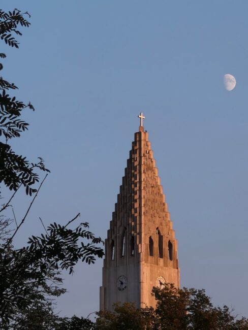 Campanario de Islandia con la luna al atardecer Campanario de una iglesia en Islandia al atardecer con la luna creciente en el cielo.