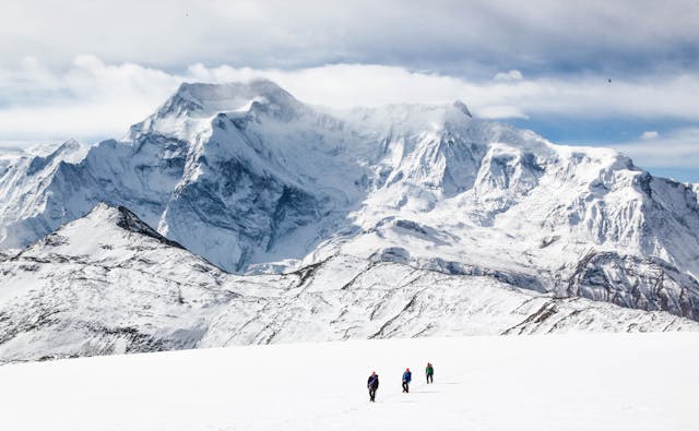 Montañistas caminando sobre la nieve frente a una montaña del Himalaya