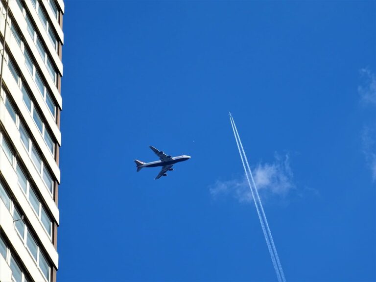Avión sobrevolando edificio con cielo azul y estela de condensación