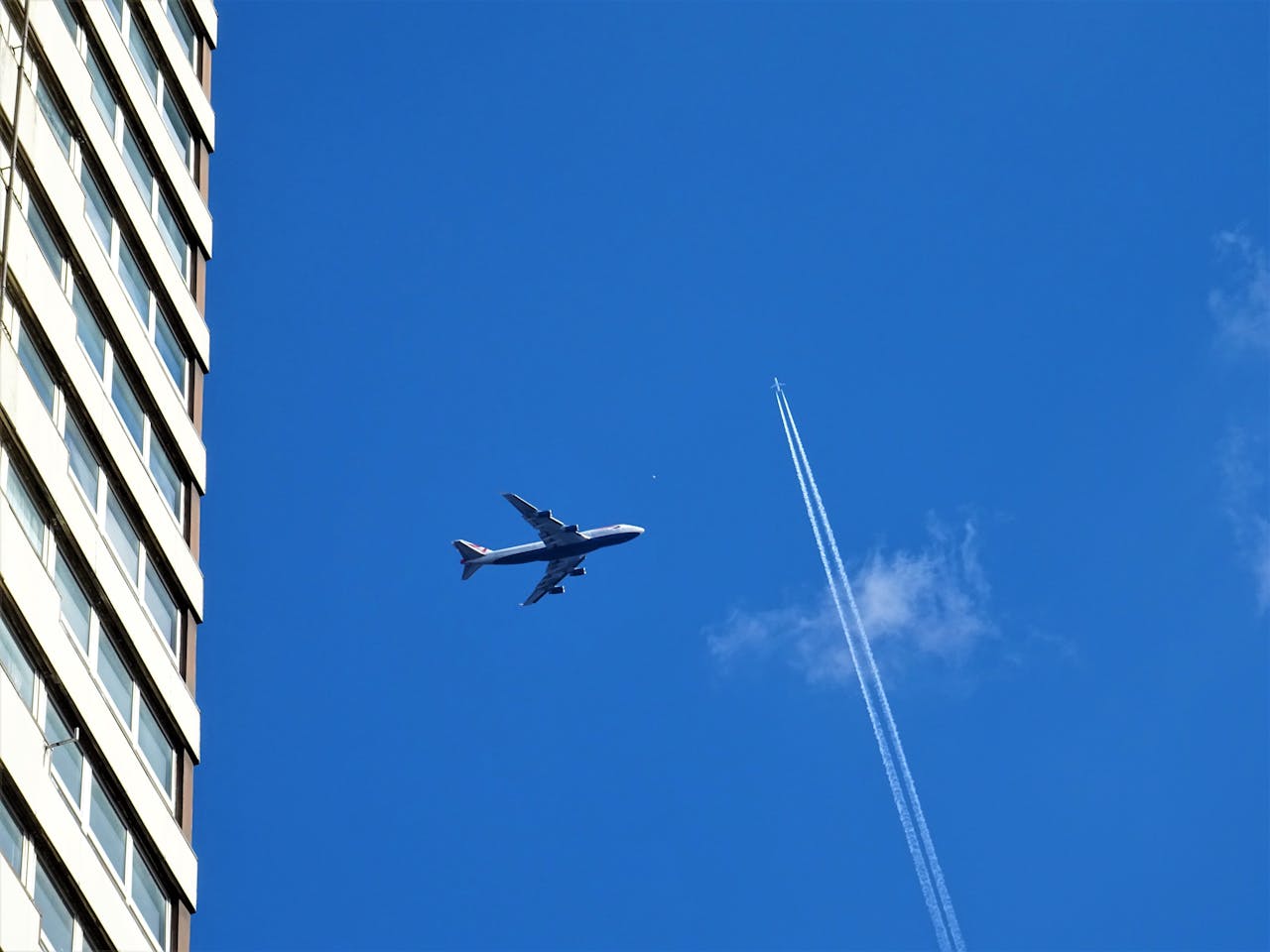 Avión sobrevolando edificio con cielo azul y estela de condensación