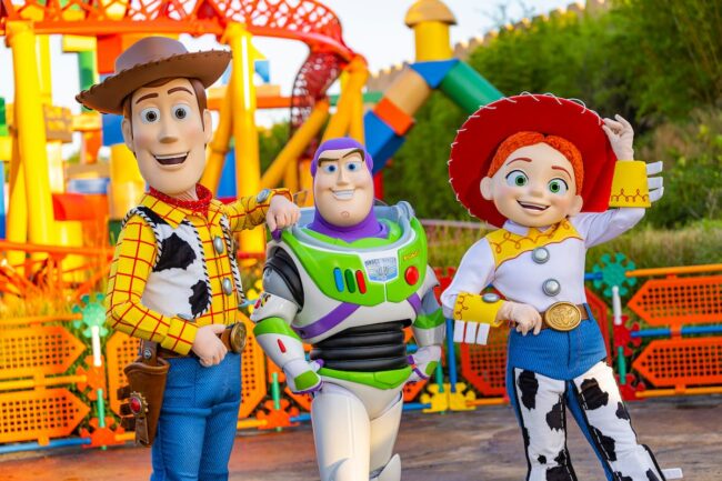 Woody, Buzz Lightyear y Jessie posan sonrientes en Toy Story Land en Disney, invitando a vivir una experiencia mágica.