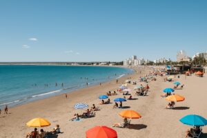 Vista panorámica de la playa de Puerto Madryn en verano, con arena clara, mar calmo y personas disfrutando del sol en la Patagonia argentina.