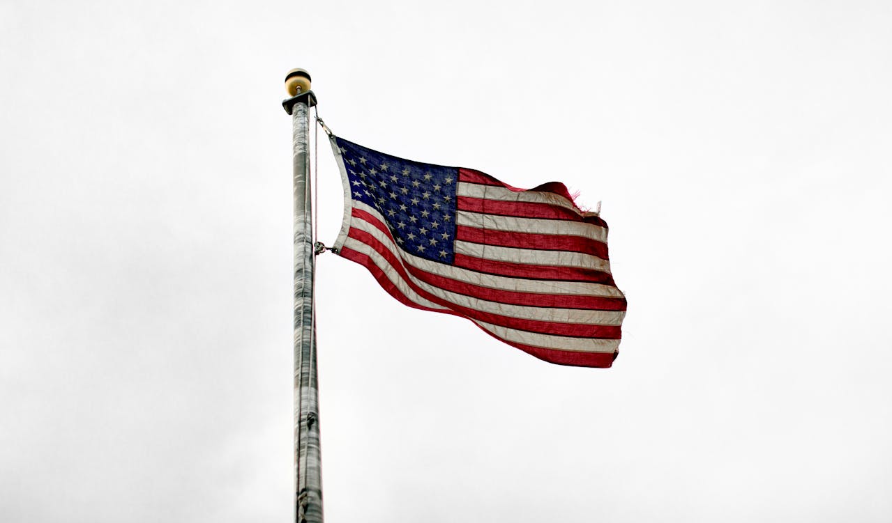 Bandera de Estados Unidos ondeando sobre un fondo gris claro.