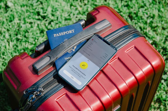 Maleta roja con pasaporte y teléfono móvil sobre el pasto, simbolizando los nuevos cambios en las normas del equipaje de mano para viajar.