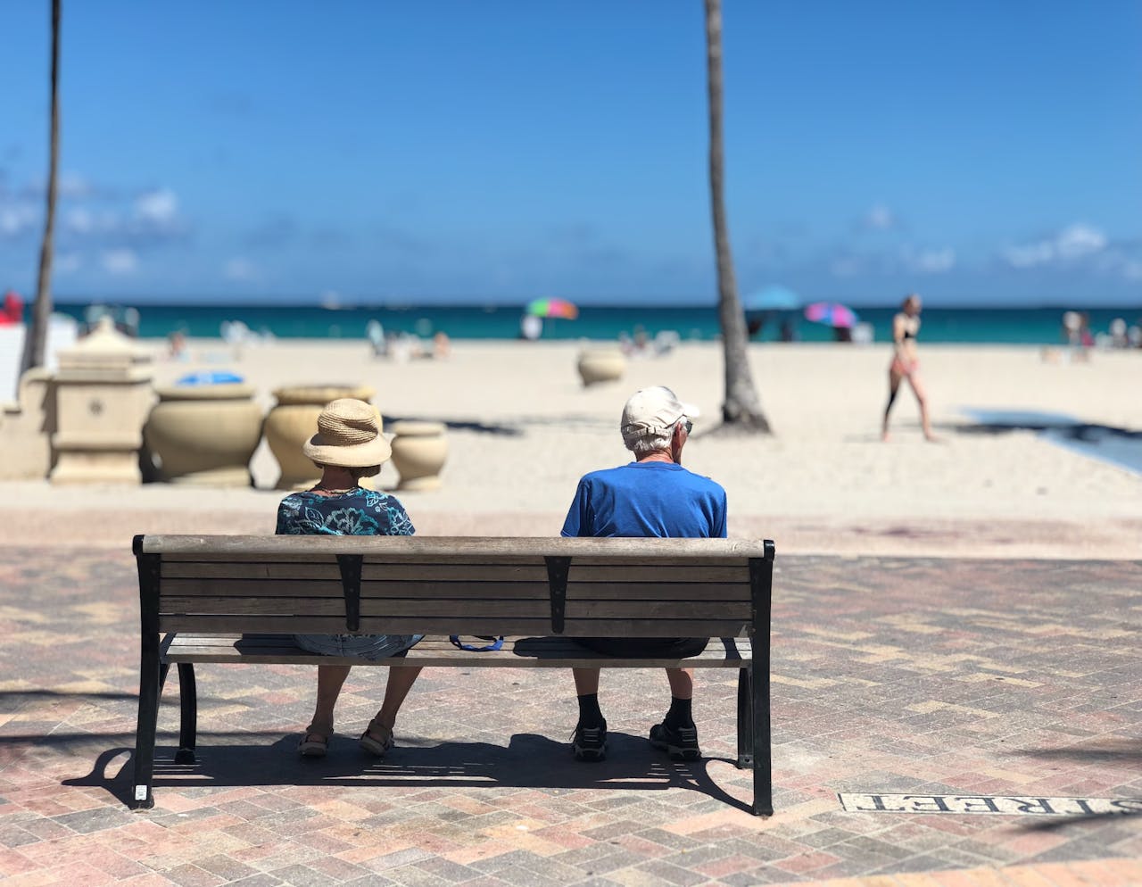 Pareja de turistas mayores sentados frente al mar en un día soleado, disfrutando de unas vacaciones relajadas en la playa.