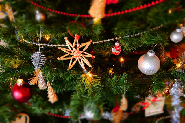 Adornos navideños colgados en un árbol de Navidad con luces y decoraciones tradicionales.