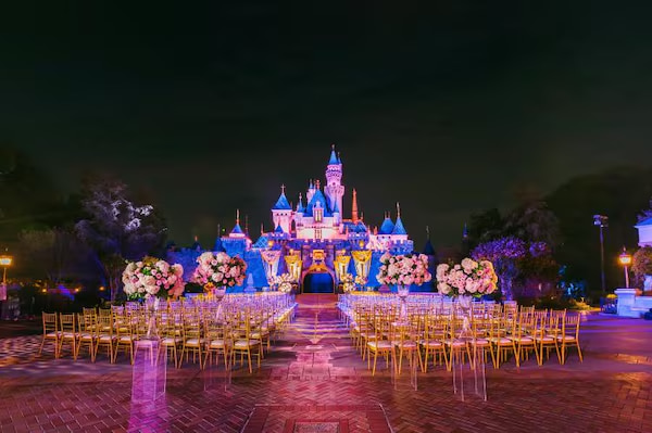 Montaje de ceremonia de boda nocturna frente al castillo de Disney con sillas y decoración floral