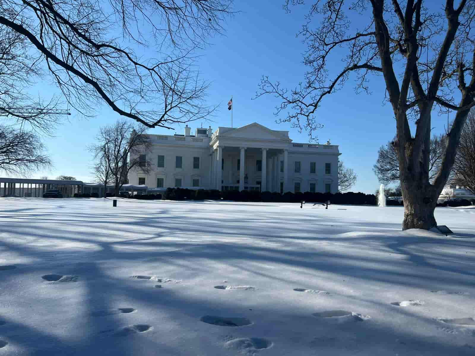 La Casa Blanca cubierta de nieve en Washington DC con árboles sin hojas y cielo despejado