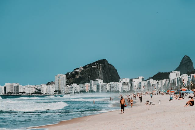 Playa de Copacabana en Río de Janeiro con edificios frente al mar y el Pan de Azúcar al fondo, una de las mejores zonas donde hospedarse en 2026