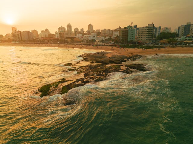 Costa urbana de Brasil al atardecer con playa, mar y edificios frente al océano, imagen comparativa Brasil vs Caribe en 2026.