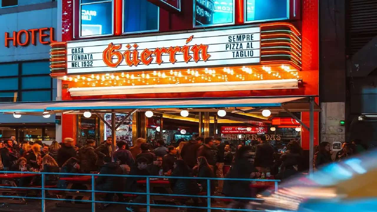 Pizzería Guerrin de noche en Buenos Aires con gran cantidad de gente y su clásica fachada iluminada