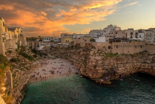 Cala Lama Monachile en Polignano a Mare con playa entre acantilados al atardecer en Puglia, Italia.