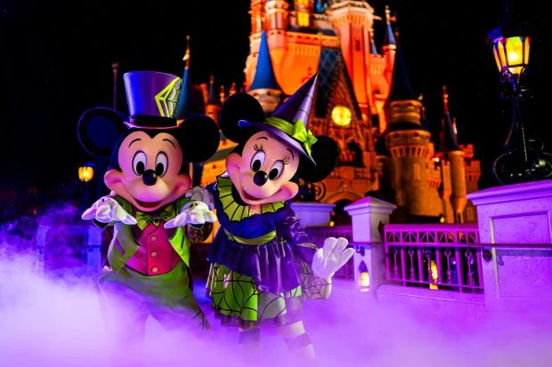 Mickey y Minnie disfrazados de Halloween frente al castillo de Magic Kingdom de noche.