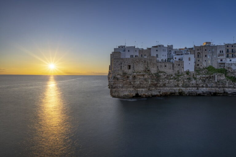Polignano a Mare al atardecer con casas sobre acantilados frente al mar Adri&aacute;tico en Puglia, Italia.