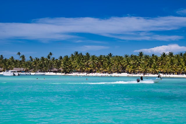 Mar turquesa y playa tropical de Punta Cana con palmeras y lancha en un día soleado.