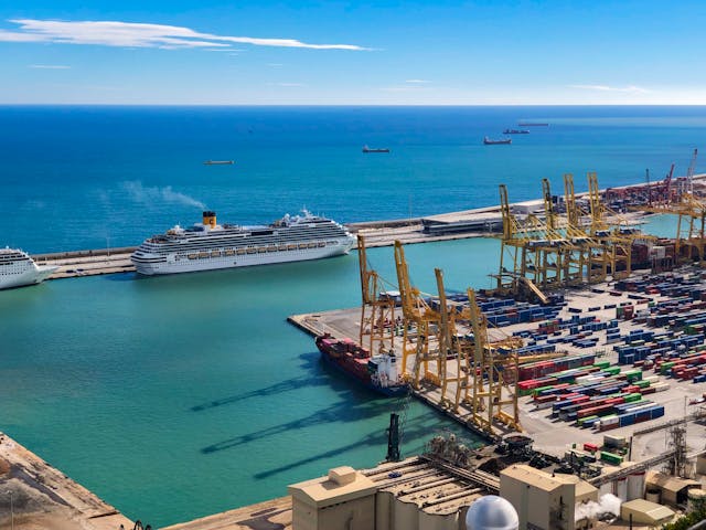 Crucero atracado en el puerto de Barcelona junto a grúas y contenedores, una imagen que representa las nuevas medidas para ordenar el turismo de cruceros y cobrar una tasa a visitantes.