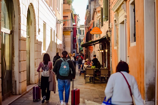 Viajeros caminando con valijas por una calle peatonal de Venecia, una ciudad ideal para recorrer sin auto.