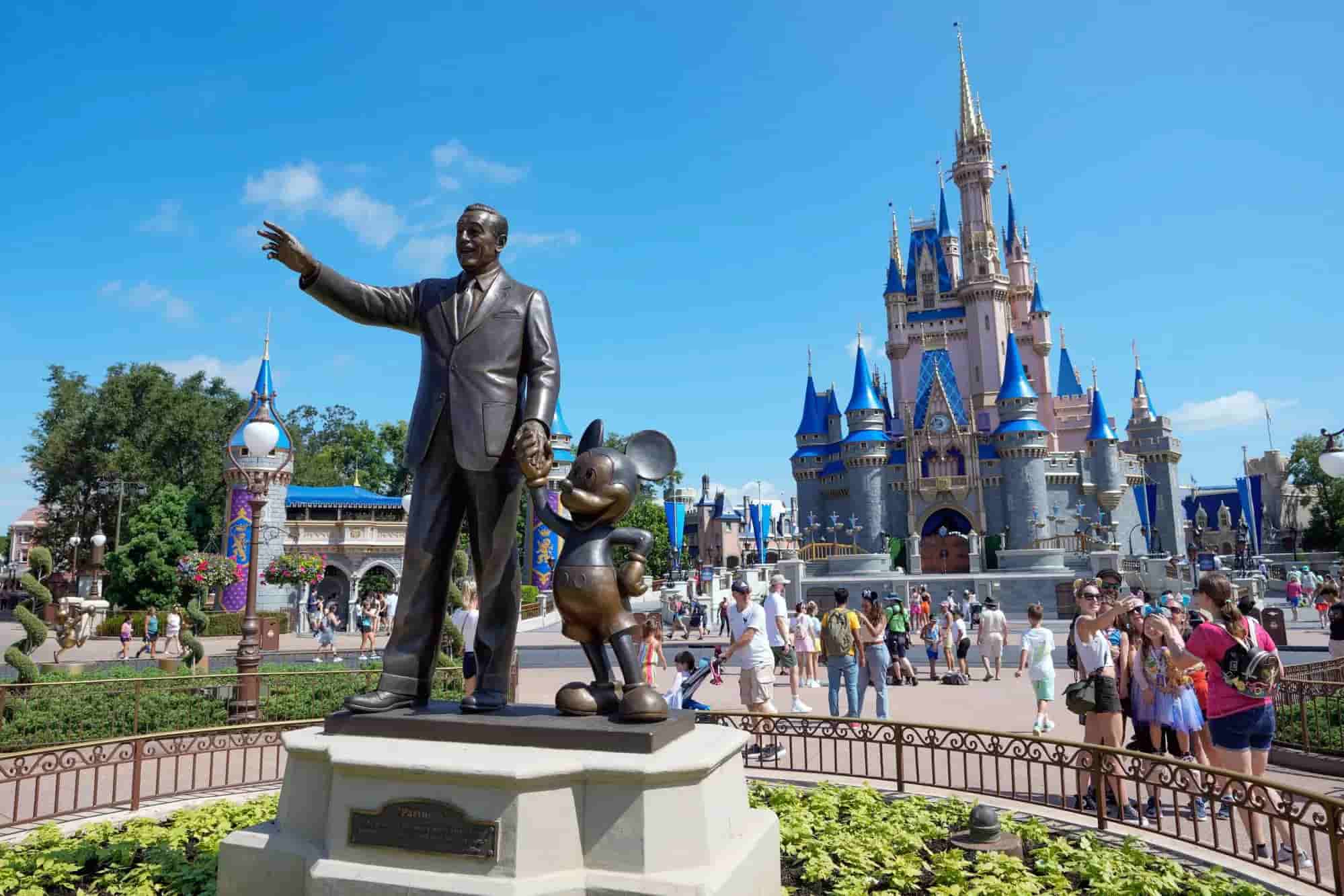 Castillo de Cenicienta en Magic Kingdom con visitantes frente a la estatua de Walt Disney y Mickey Mouse en Walt Disney World.