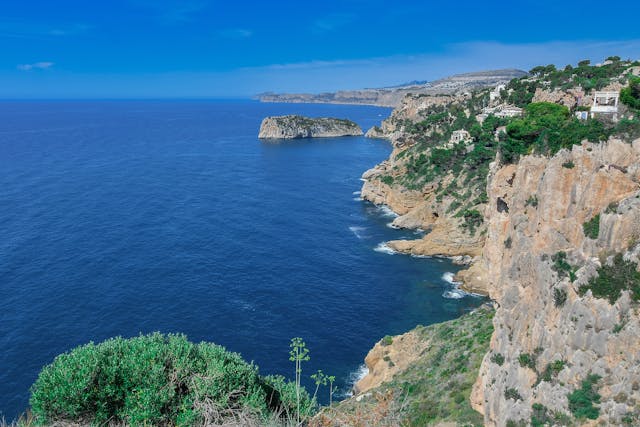 Dónde queda Ibiza: ubicación y cómo llegar a la isla Vista de la costa rocosa de Ibiza frente al mar Mediterráneo, una imagen ideal para ilustrar dónde queda la isla, su ubicación en España y cómo llegar.