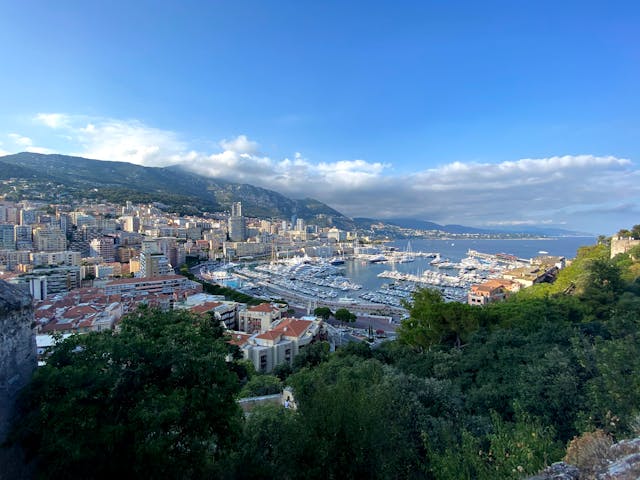 Vista panorámica de Mónaco con el puerto, edificios sobre la costa, montañas y el mar Mediterráneo.