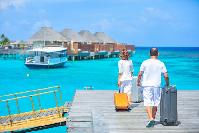 Pareja llegando a un resort sobre el mar con valijas, en una imagen asociada a paquetes turísticos y promociones de viajes.