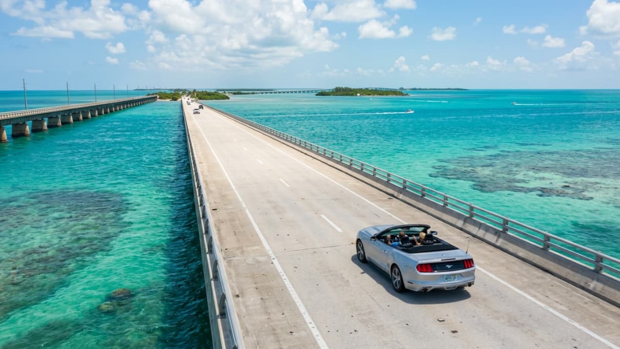 Auto recorriendo un puente sobre aguas turquesas en la ruta de Miami a Key West, una imagen que muestra el viaje por la Overseas Highway y la distancia entre ambos destinos de Florida.