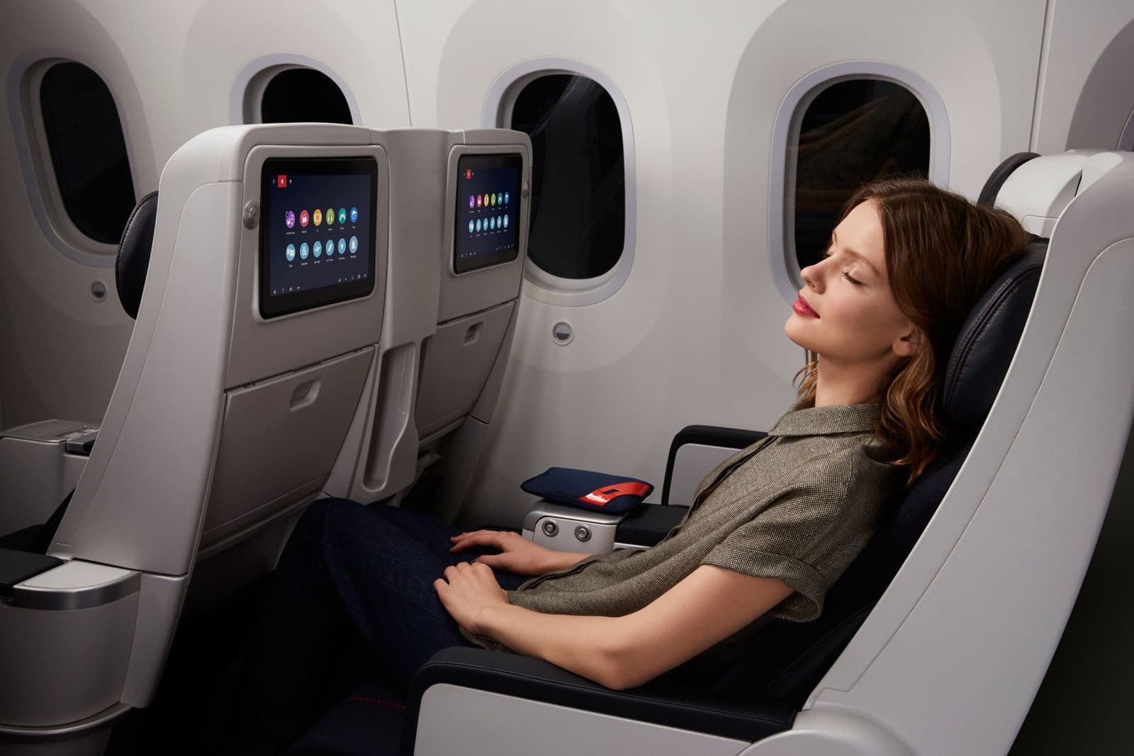 Pasajera descansando en asiento reclinable de avión con pantalla individual y mayor comodidad en premium economy