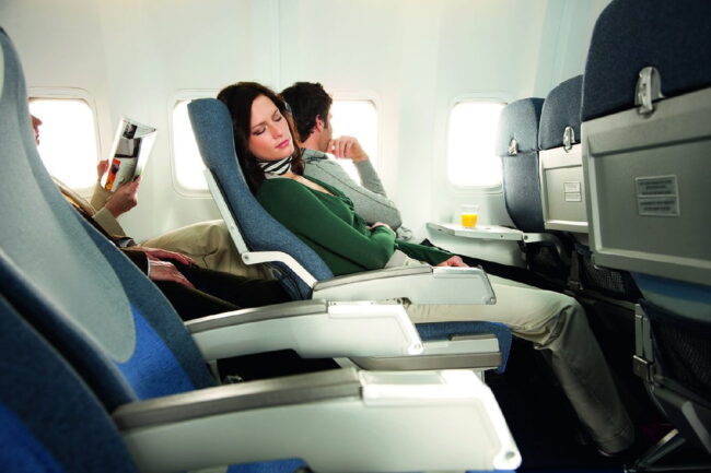 Pasajera descansando en asiento amplio de avión, con más espacio para piernas en clase premium economy