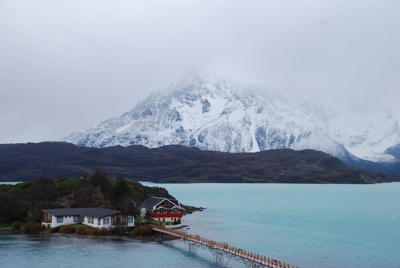 Lago de color turquesa con montañas nevadas y cabañas en la Patagonia chilena, una imagen que representa los paisajes ideales para unas vacaciones de invierno en Chile.
