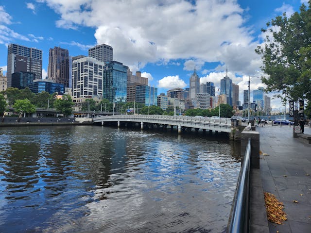 Vista urbana de Melborune junto a un río con paseo peatonal, ideal para recorrer una ciudad en bicicleta.