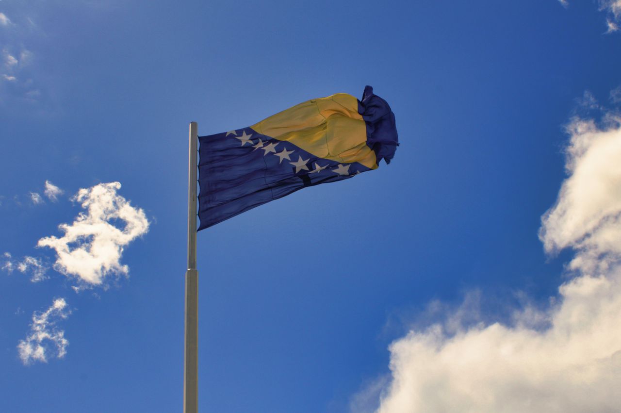 Bandera de Bosnia y Herzegovina ondeando sobre cielo azul, imagen útil para ubicar el país en los Balcanes.