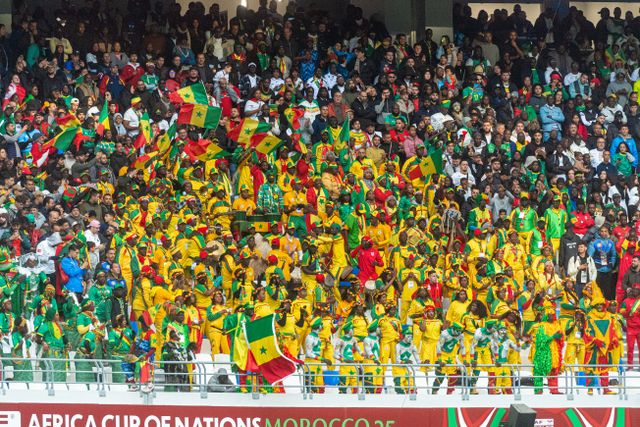 Hinchas de Senegal con banderas verdes, amarillas y rojas en un estadio, imagen relacionada con la cultura y la identidad del país.