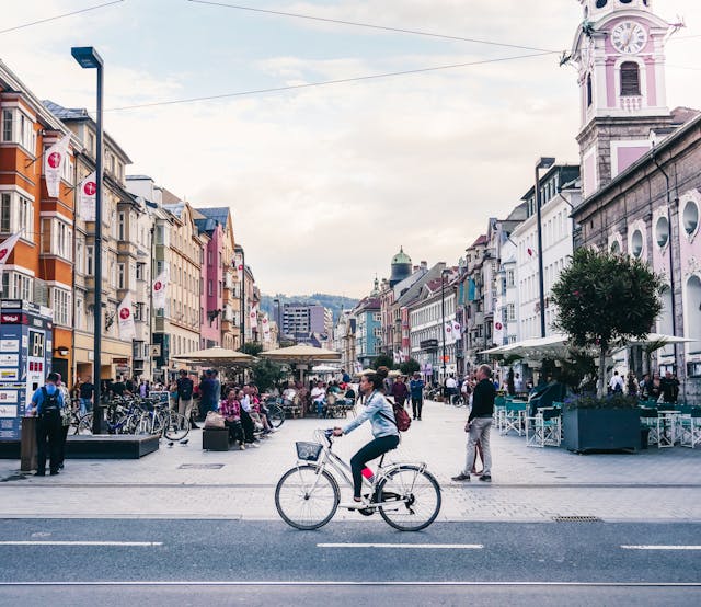 Persona en bicicleta por una calle peatonal de una ciudad europea, imagen asociada a calidad de vida y movilidad urbana.