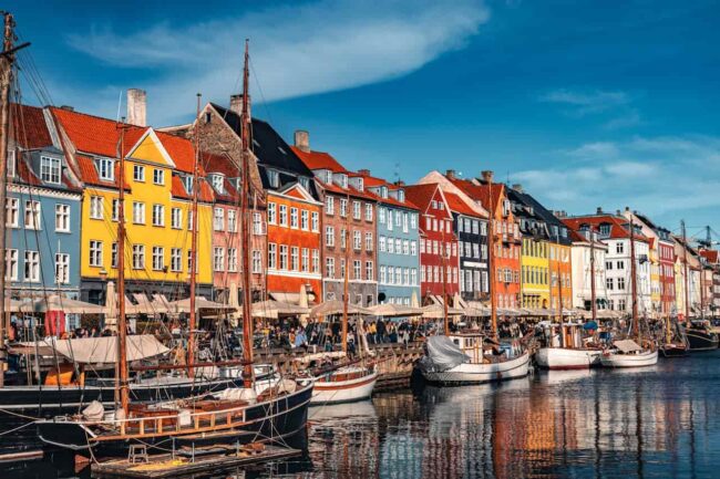 Canal de Nyhavn en Copenhague con casas de colores, barcos y terrazas, una imagen asociada a calidad de vida urbana.
