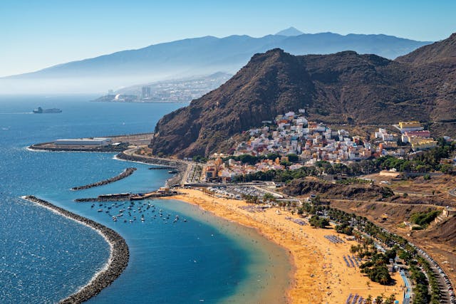 Vista aérea de una extensa playa en Tenerife, con arena dorada, mar azul y montañas junto a la costa.