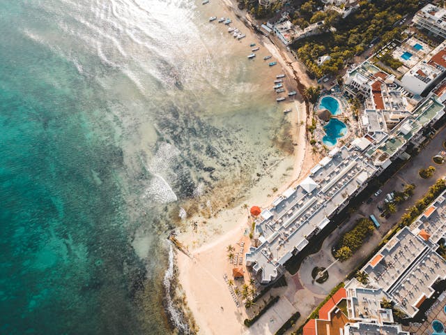 Vista aérea de una playa de Playa del Carmen con mar turquesa, hoteles frente al mar y embarcaciones cerca de la costa.