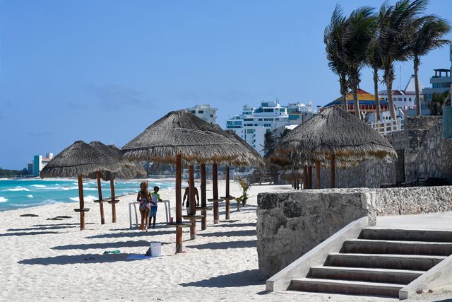 Playa de Playa del Carmen con palapas, arena blanca, mar Caribe y hoteles frente a la costa.