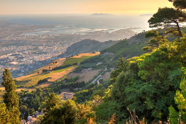Vista panorámica de Sicilia, en Italia, con montañas, costa, ciudad y mar al atardecer.