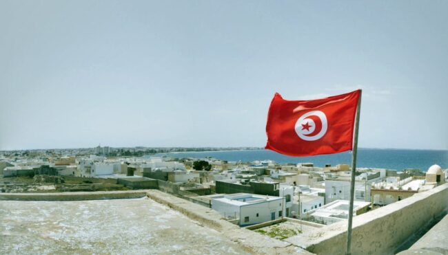 Bandera de T&uacute;nez ondeando sobre una ciudad costera junto al mar Mediterr&aacute;neo.