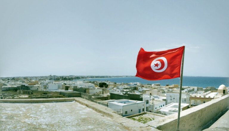 Bandera de Túnez ondeando sobre una ciudad costera junto al mar Mediterráneo.