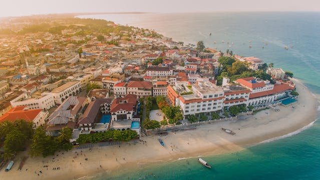 Vista aérea de Zanzíbar con playa, edificios frente al mar y aguas turquesas, una de las islas más lindas del mundo.