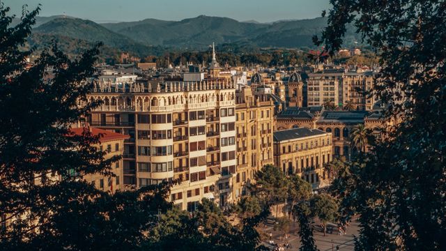 Vista del centro urbano de San Sebastián con edificios históricos y montañas del País Vasco al fondo.