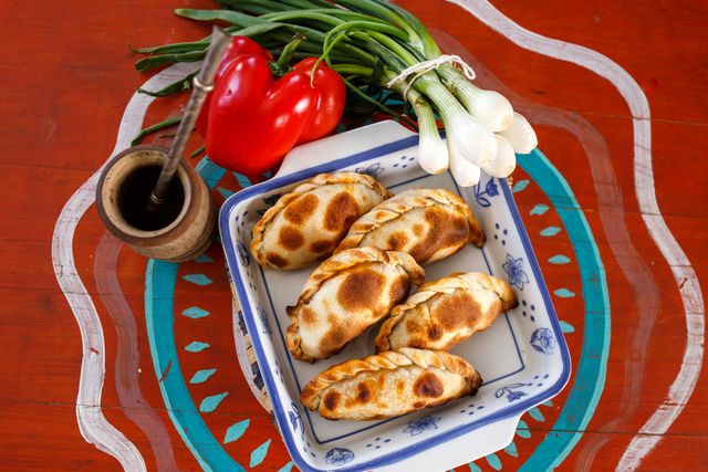 Empanadas argentinas servidas con mate, pimientos y cebolla de verdeo, imagen relacionada con comidas típicas regionales de Argentina.