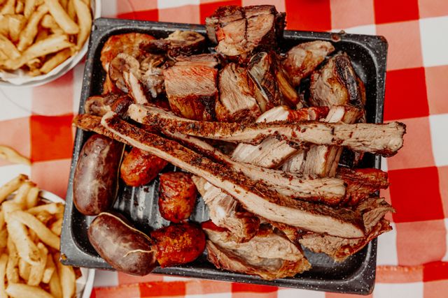 Parrillada argentina con distintos cortes de carne, chorizos, morcillas y papas fritas sobre una mesa de mantel a cuadros.