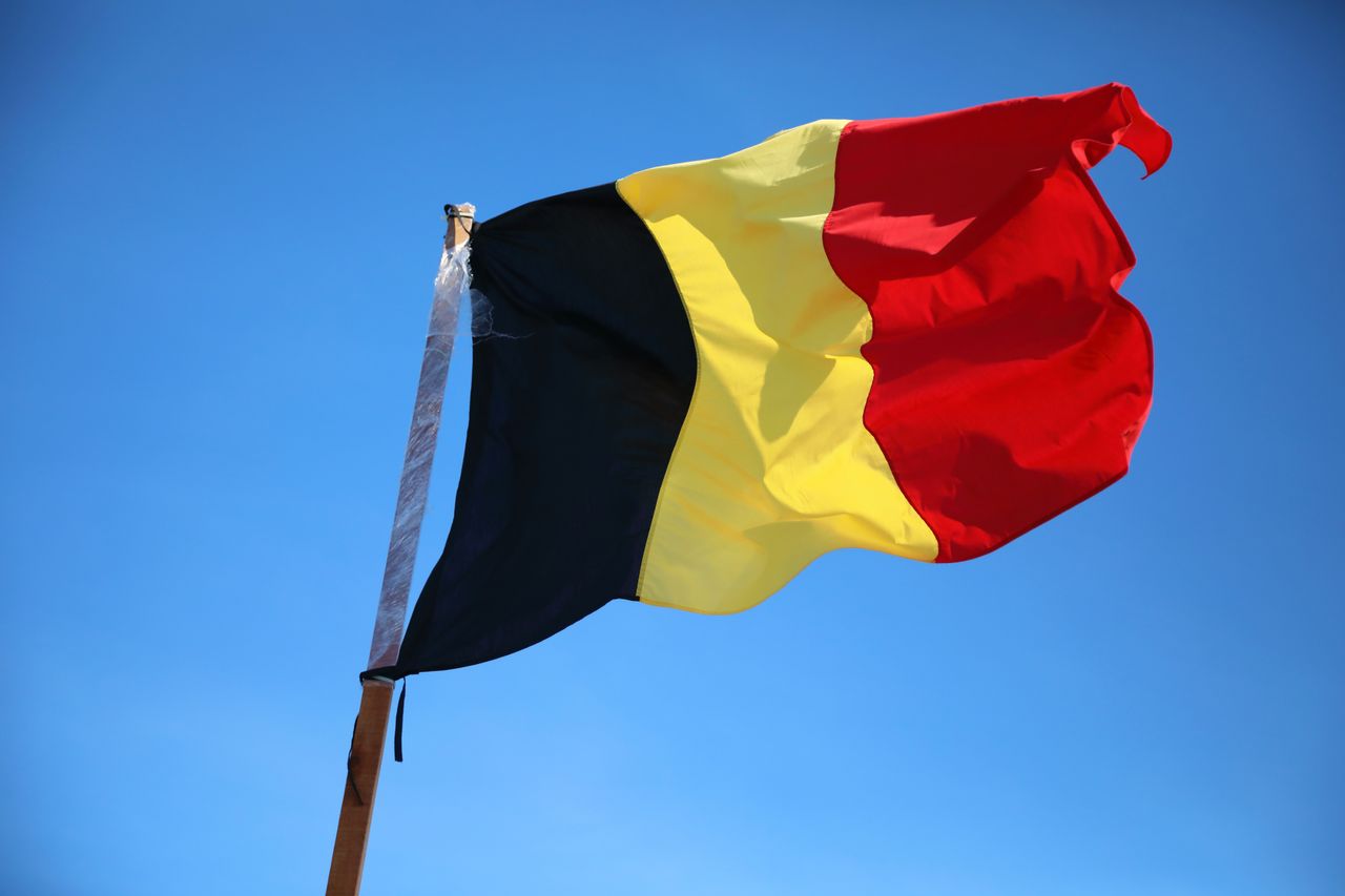 Bandera de Bélgica ondeando sobre cielo azul, imagen relacionada con una guía sobre dónde queda Bélgica en Europa.