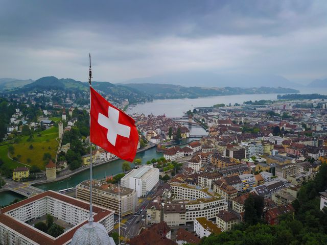 Bandera de Suiza sobre una vista panorámica de Lucerna, con lago, ciudad histórica y montañas al fondo.