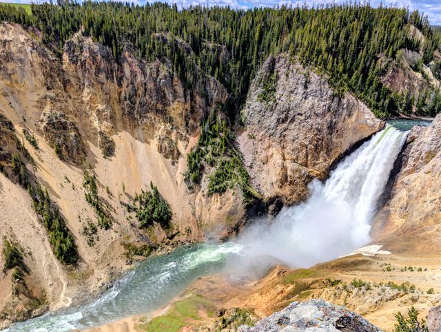 Cascada en el Gran Cañón de Yellowstone, con paredes rocosas, río y bosque de pinos alrededor.