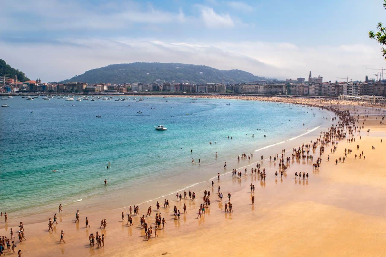 Vista panorámica de la playa de La Concha con bañistas, embarcaciones y el centro de San Sebastián frente a la bahía.